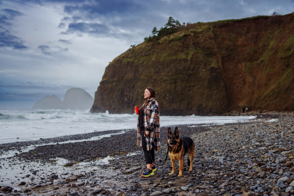 Woman dressed in warm clothes standing on Oregon Coast beach with her dog